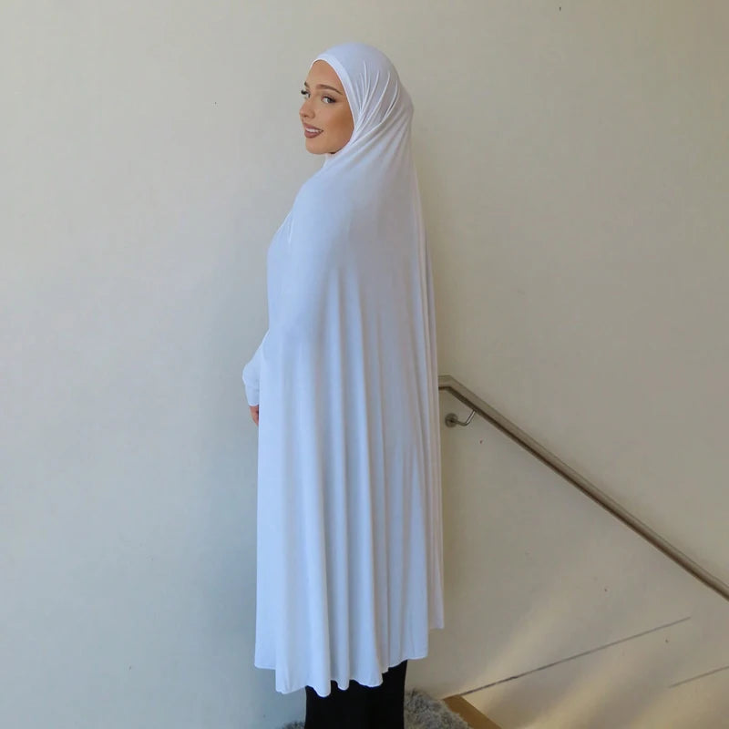 Eine Frau trägt eine elegante weiße Baumwoll-Abaya mit Ärmeln und Hijab, vor einer hellen Wand stehend.