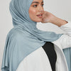 Eine Frau trägt einen einfarbigen hellblauen Jersey-Hijabschal mit einem weiß-schwarzen Outfit.