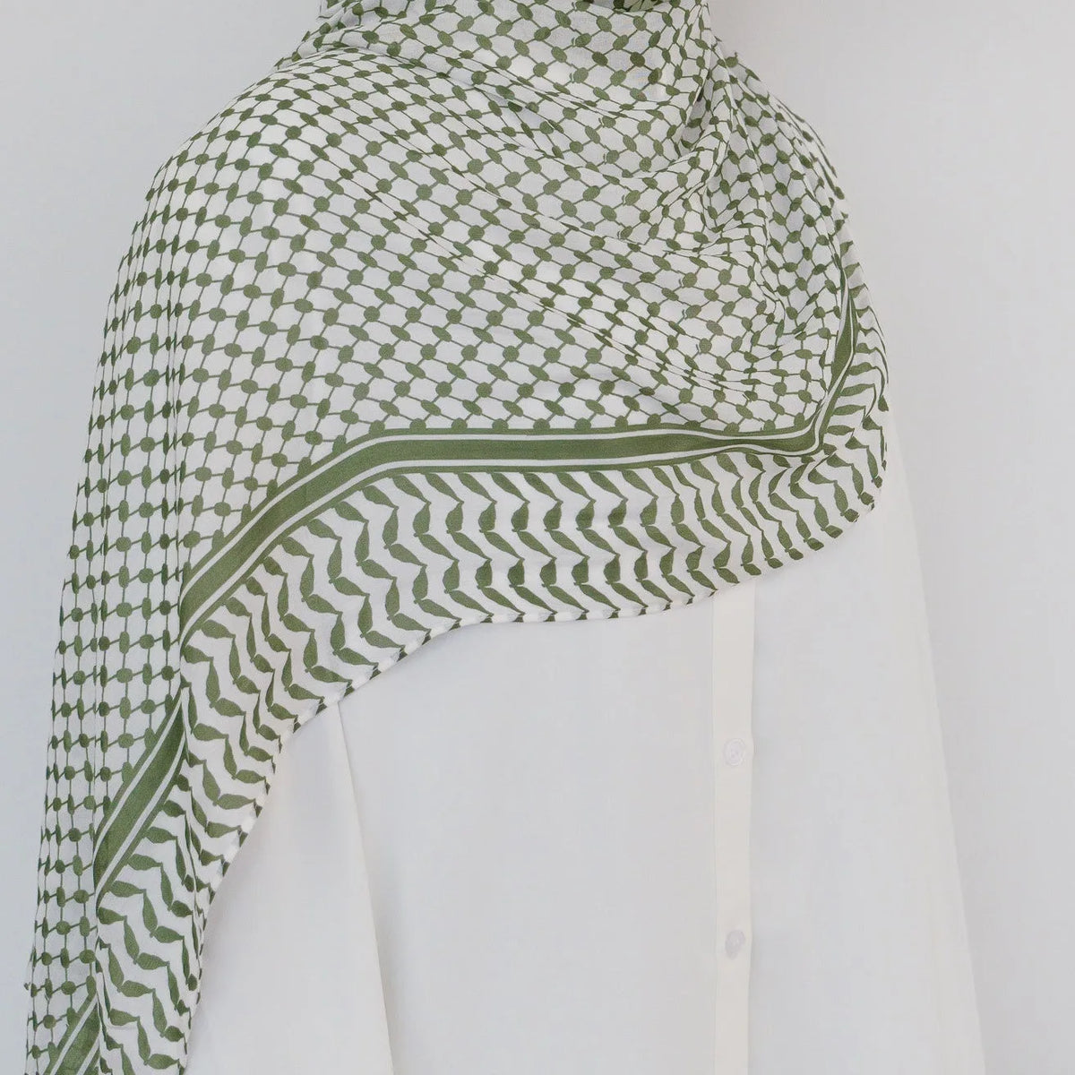 Primer plano de un elegante hiyab de chifón verde oliva drapeado sobre una prenda blanca.