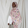 A woman wearing a watercolor printed pink scarf hijab against a light background.