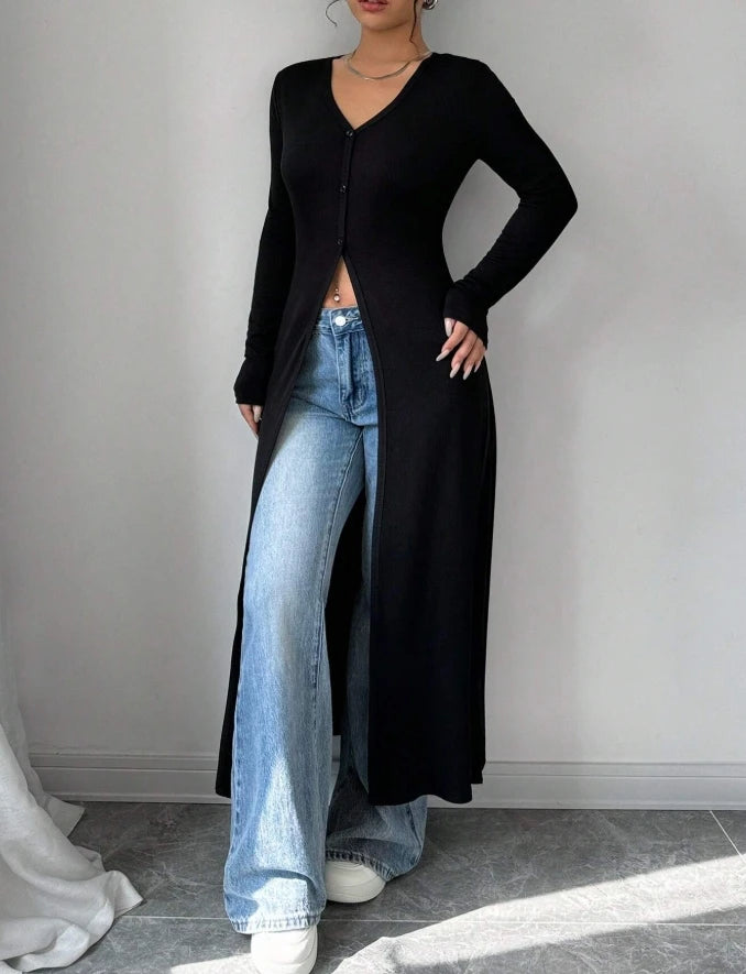 Eine Frau trägt einen schwarzen gerippten Strick-Maxi-Cardigan über hellgewaschene Jeans und weiße Sneaker.
