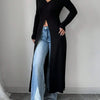 Eine Frau trägt einen schwarzen gerippten Strick-Maxi-Cardigan über helle Jeans und weiße Sneaker.