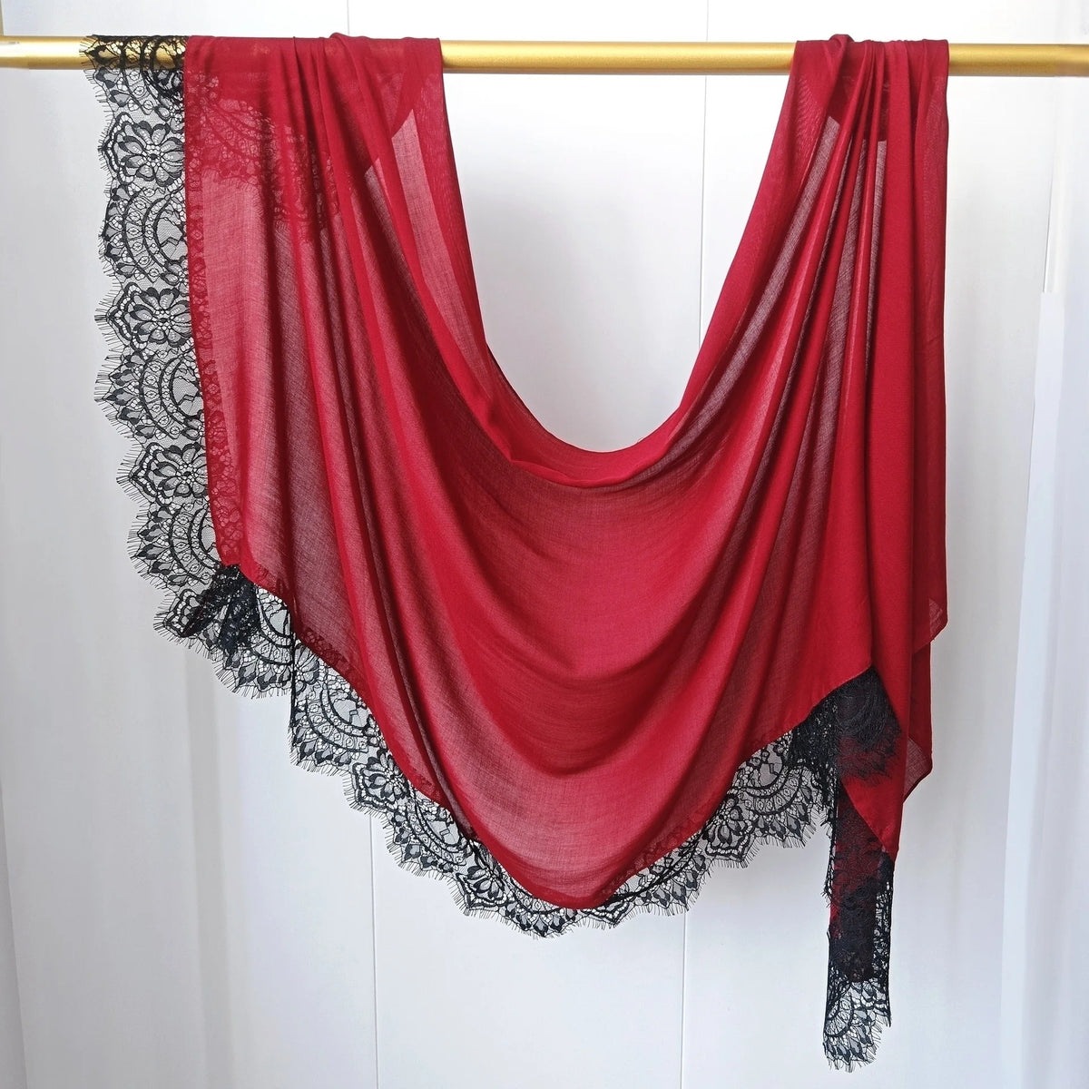 Hijab de encaje rojo intenso, estampado doble cara, drapeado sobre un varilla de madera.