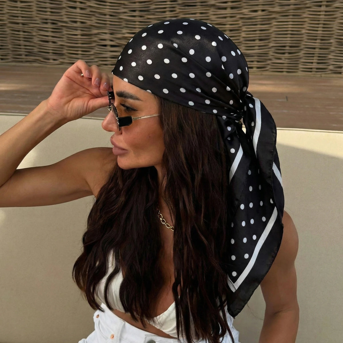A woman wearing a black and white polka dot silk scarf tied around her hair and neck.