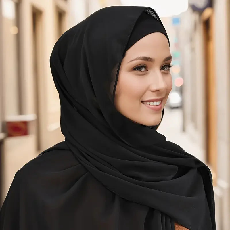 Eine Frau trägt ein schwarzes, zweiteiliges Ballon-Chiffon-Hijab-Set und lächelt und blickt zur Seite.