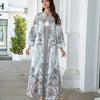 Une femme portant une élégante abaya longue perlée de diamants à motif floral blanc et bleu, debout à l'extérieur.