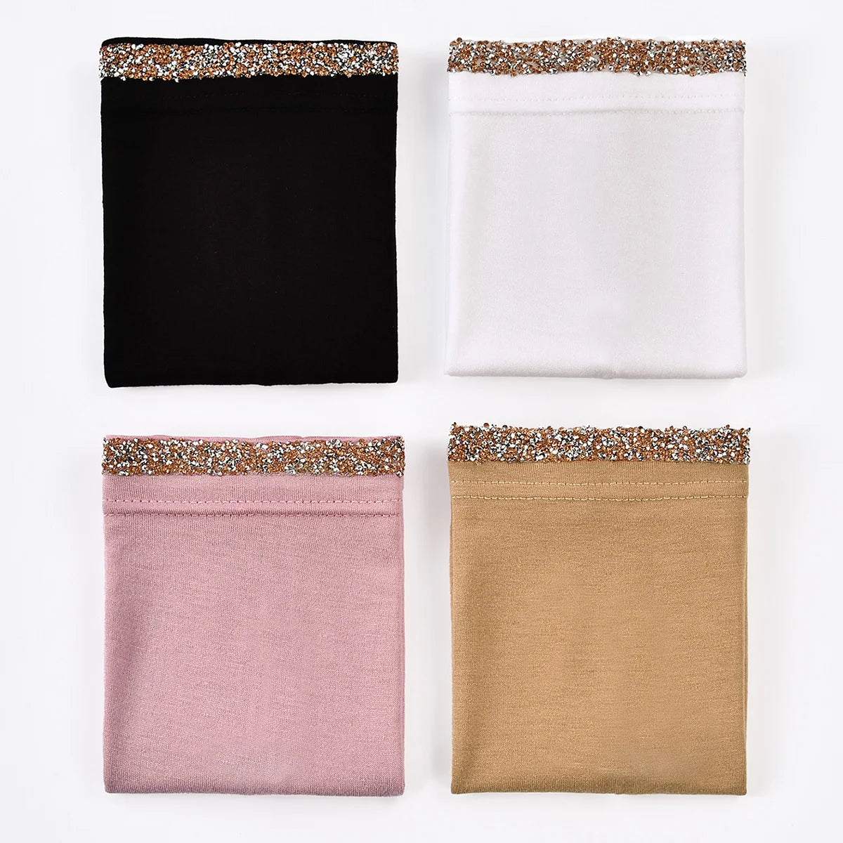 Cuatro pañuelos interiores doblados en negro, blanco, rosa y beige con ribete de purpurina dorada.