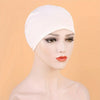 A model wearing a white classic stretch jersey turban cap against a light orange background.