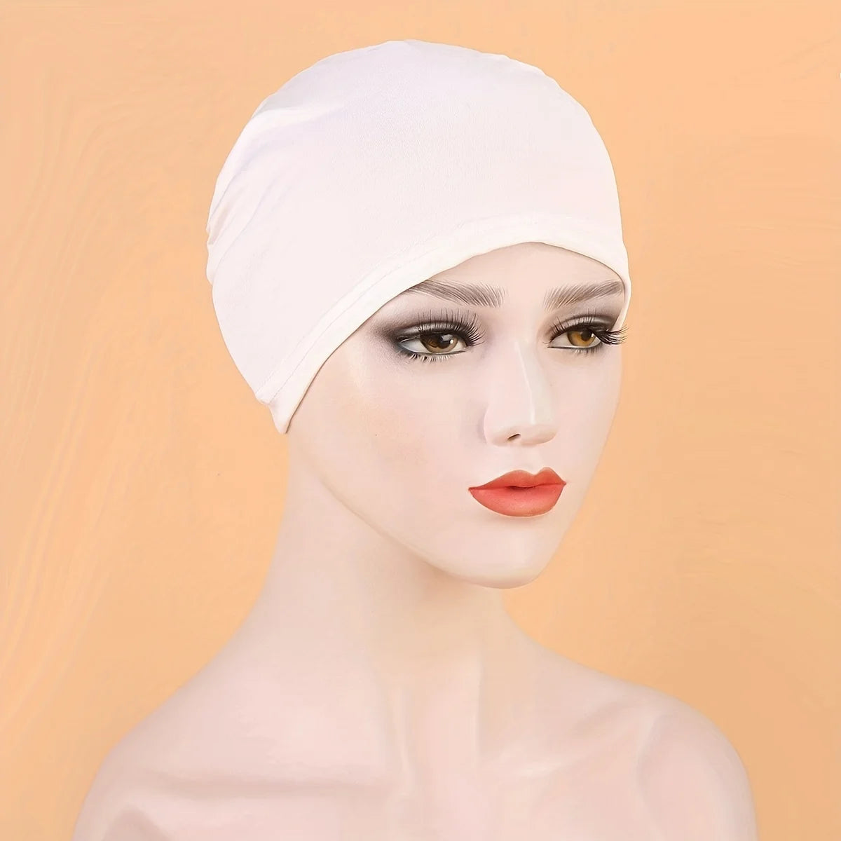 A model wearing a white classic stretch jersey turban cap against a light orange background.