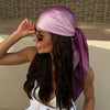 A woman wearing a purple silk scarf tied around her head and neck, with long dark hair visible.