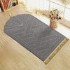 Alfombra de oración gris con patrones geométricos grabados y borlas decorativas doradas sobre un suelo de madera.