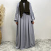 Eine Frau in einem langen, fließenden, hellgrauen islamischen Kleid und einem dunkelgrünen Schal.