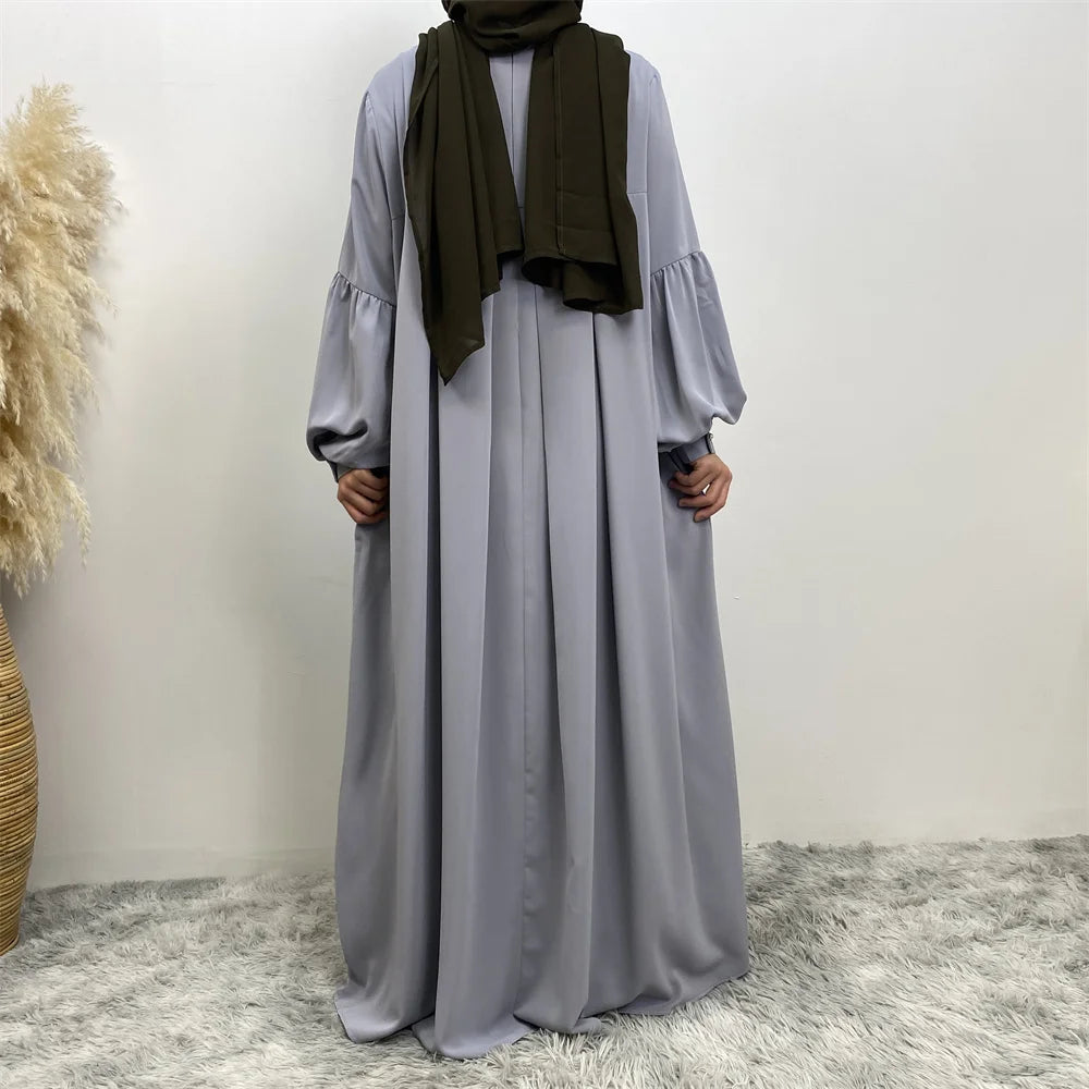 Eine Frau in einem langen, fließenden, hellgrauen islamischen Kleid und einem dunkelgrünen Schal.