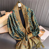 Una pashmina de lujo con patrón en verde azulado oscuro y dorado drapeada alrededor del cuello de una persona.