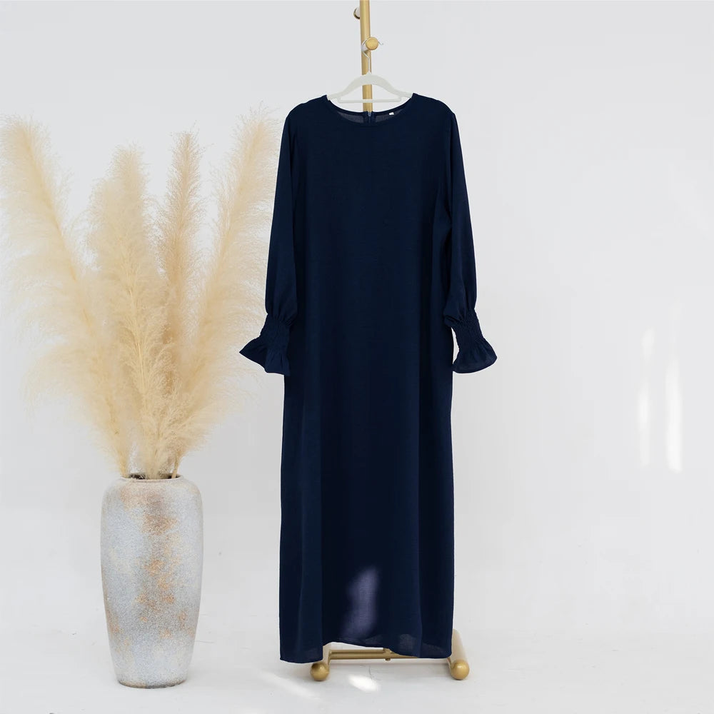 Vestido abaya azul marino de corte holgado con puños fruncidos colgado en una percha.