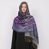 Una mujer vistiendo un pañuelo pashmina de lujo con estampado morado y verde azulado cubriendo su cabeza y hombros.