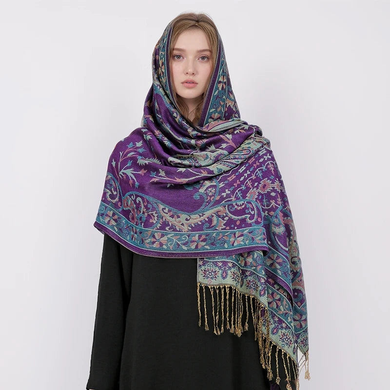 Una mujer vistiendo un pañuelo pashmina de lujo con estampado morado y verde azulado cubriendo su cabeza y hombros.
