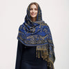 Una mujer vistiendo un pañuelo pashmina de lujo con patrón azul y dorado y bordes de flecos.