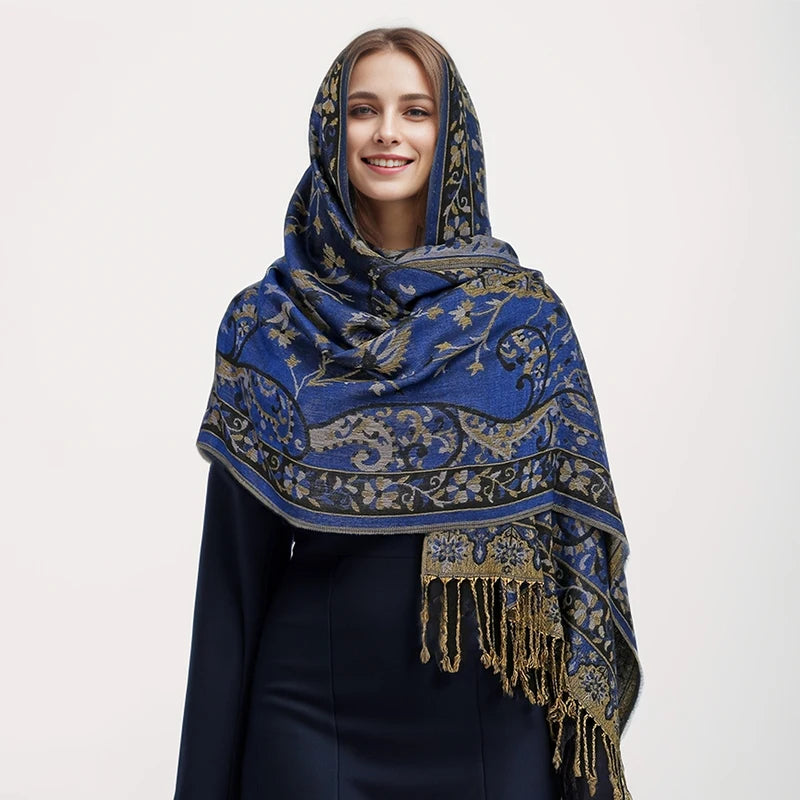 Una mujer vistiendo un pañuelo pashmina de lujo con patrón azul y dorado y bordes de flecos.