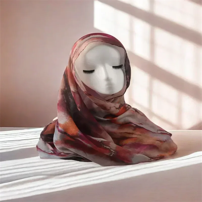 Modell trägt einen floral bedruckten Modal-Schal-Hijab in gedämpften rotbraunen Tönen, liegt auf einer weißen Oberfläche