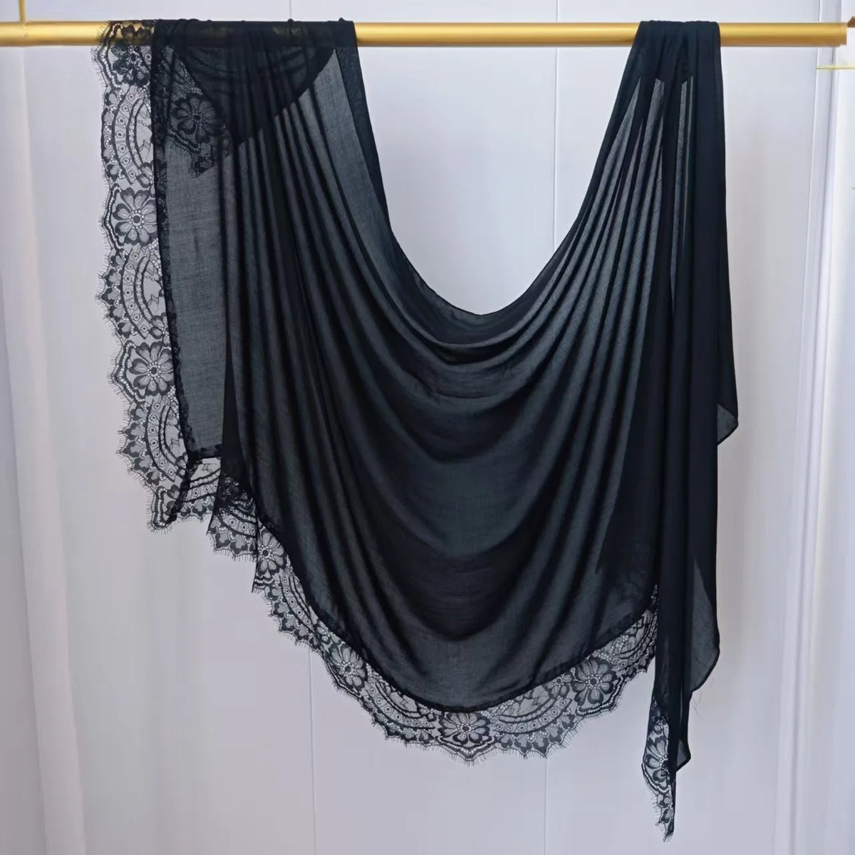 Hijab de malla negra de doble cara colgada sobre un percha de madera.