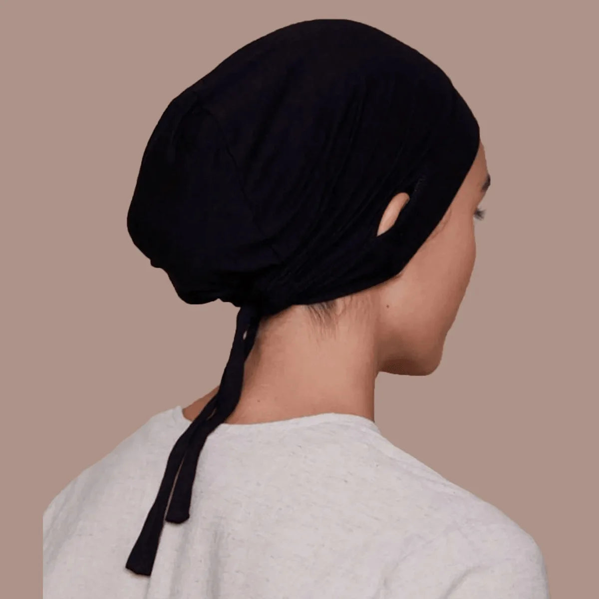 Une femme portant un bonnet inner hijab noir à cordon et un haut gris clair, vue de profil.