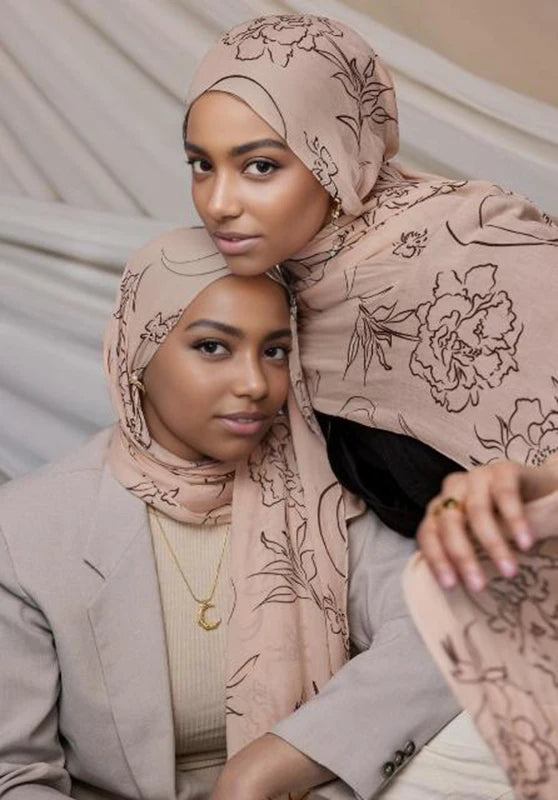 Una mujer vistiendo un hijab beige con estampado floral acuarela, mirando directamente a la cámara.