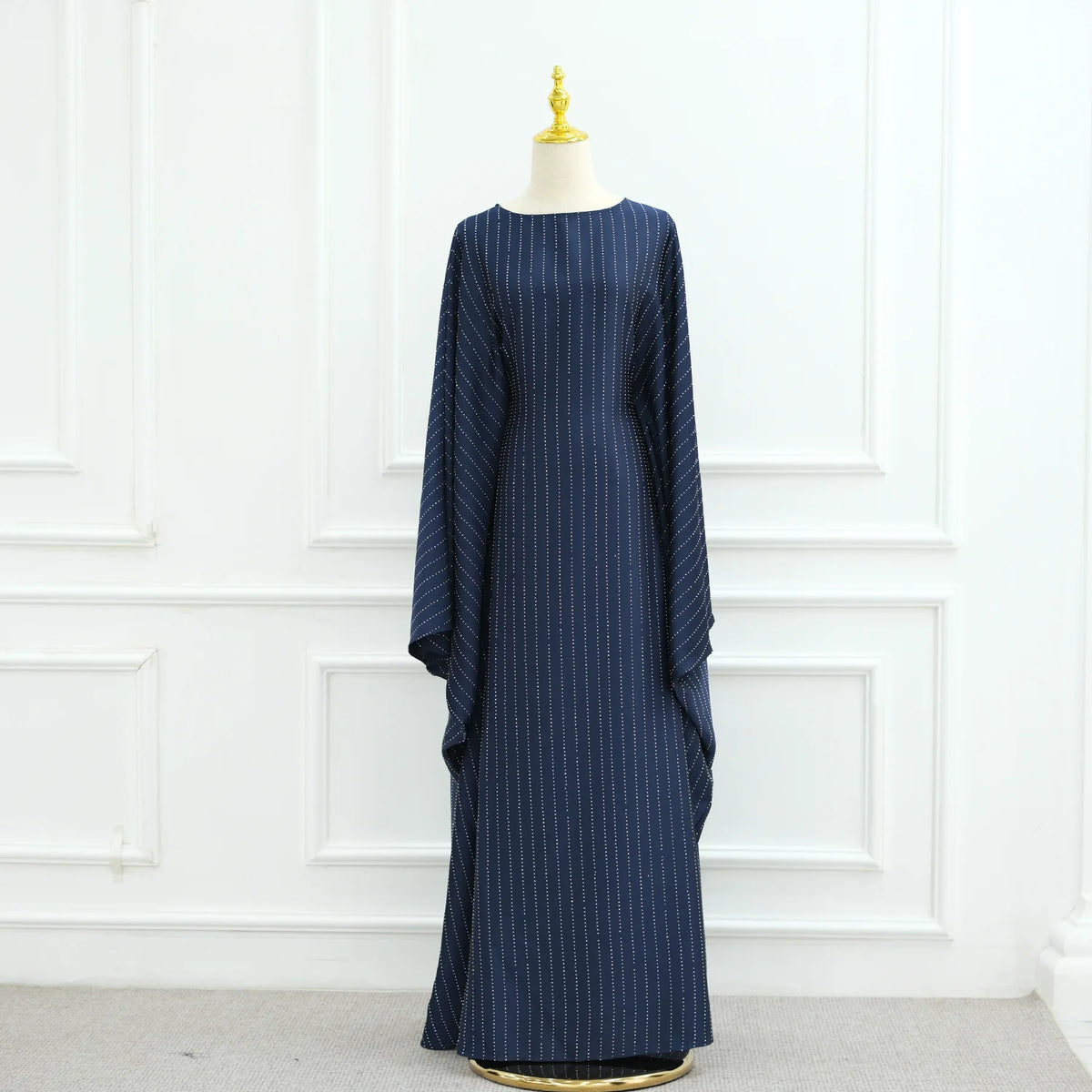 Una abaya de manga de murciélago azul marino de lujo, exhibida en un maniquí contra una pared de paneles blancos.