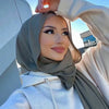 Eine Frau trägt einen eleganten, einfarbigen Chiffon-Hijab und eine helle Jacke, schaut zur Seite.