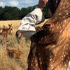Eine Frau mit braun-weißem Hijab blickt auf eine Rehherde in einem trockenen Feld.