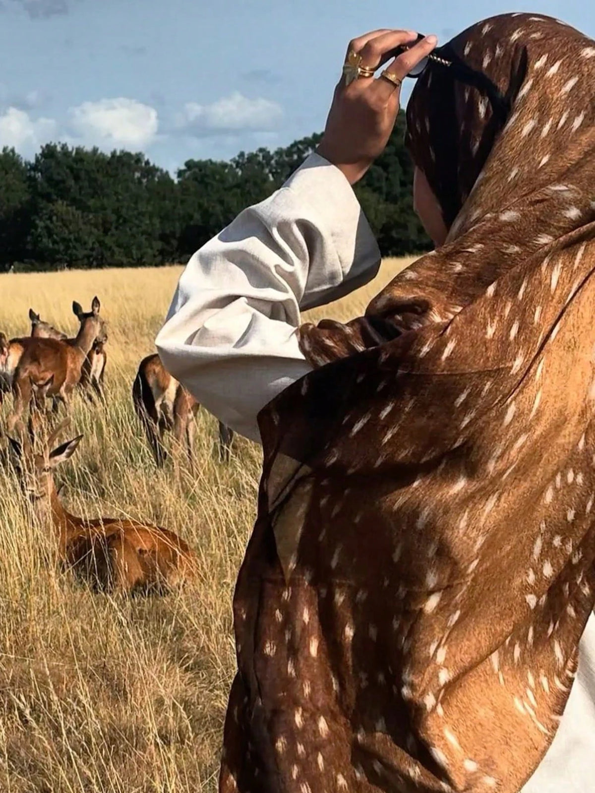 Eine Frau mit braun-weißem Hijab blickt auf eine Rehherde in einem trockenen Feld.