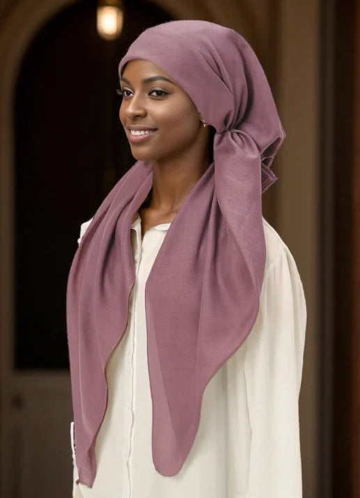 Una mujer vistiendo un hijab malva y una blusa crema, mirando hacia un lado.