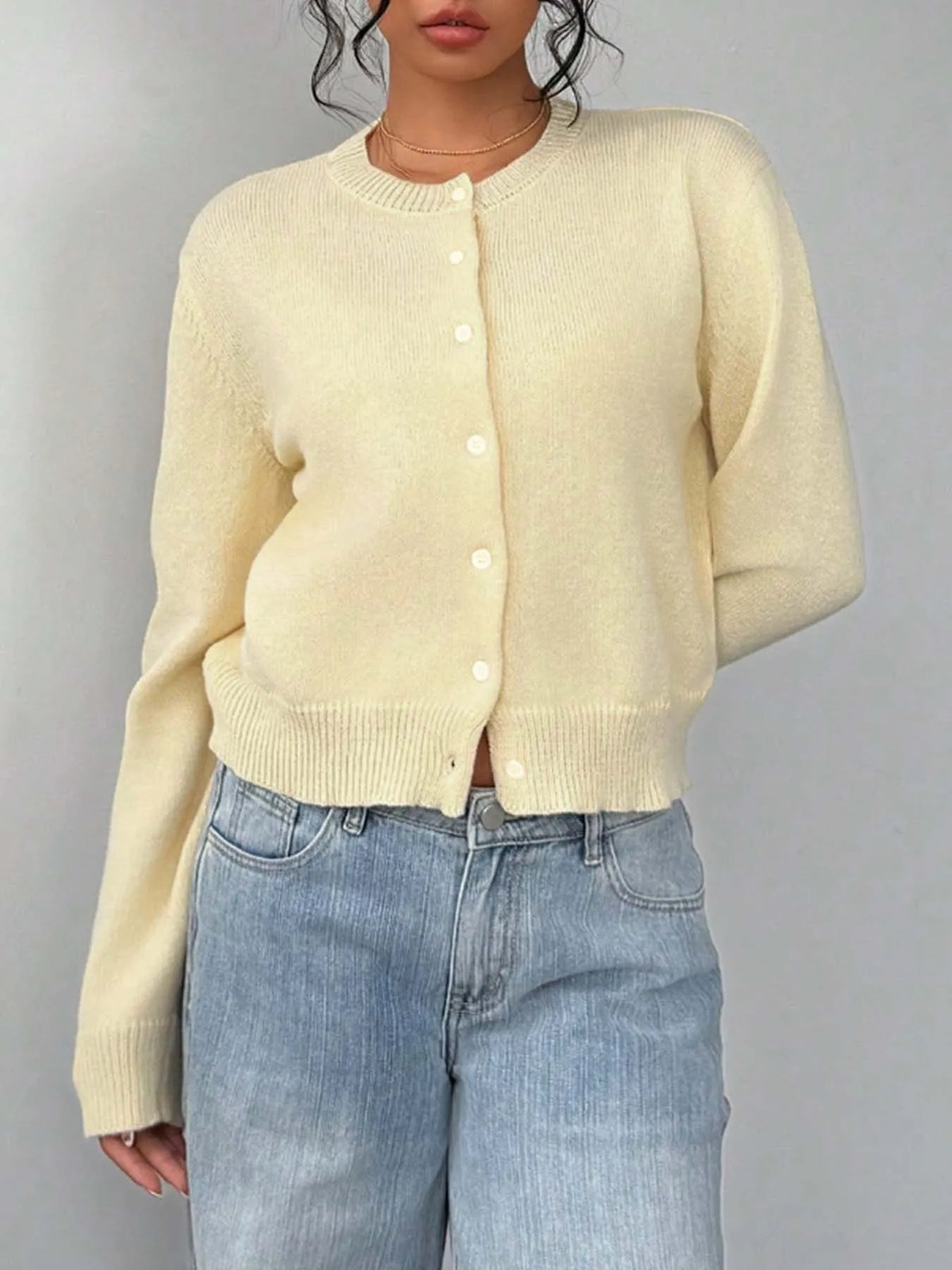 Une femme portant un pull tricoté de couleur crème et un jean délavé clair.