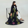 Una mujer modela un conjunto de abaya de gasa negra y verde oliva con pantalones blancos y un bolso negro.
