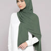 A woman wearing a solid olive green chiffon hijab and a white top.