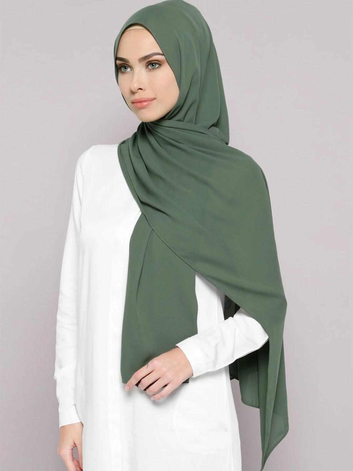 A woman wearing a solid olive green chiffon hijab and a white top.