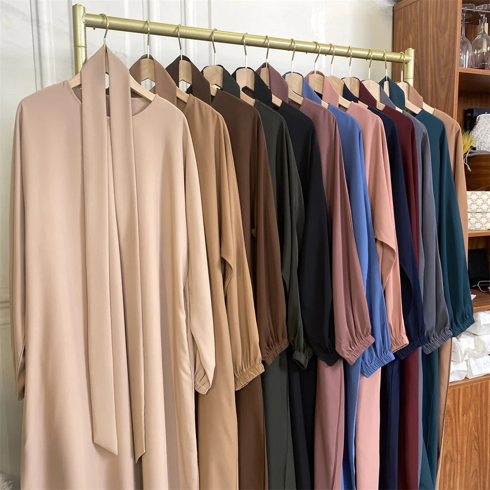 Ein Regal mit Frauen-Kaftanen und Abayas im marokkanischen Stil in Erdtönen und Blautönen, an einem Holzstab aufgehängt.