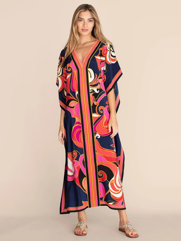 Una mujer modela un vestido caftan de playa azul marino con vibrantes estampados florales y a rayas.