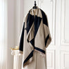 Pañuelo pashmina geométrico beige y negro colgado en una percha contra una pared blanca.