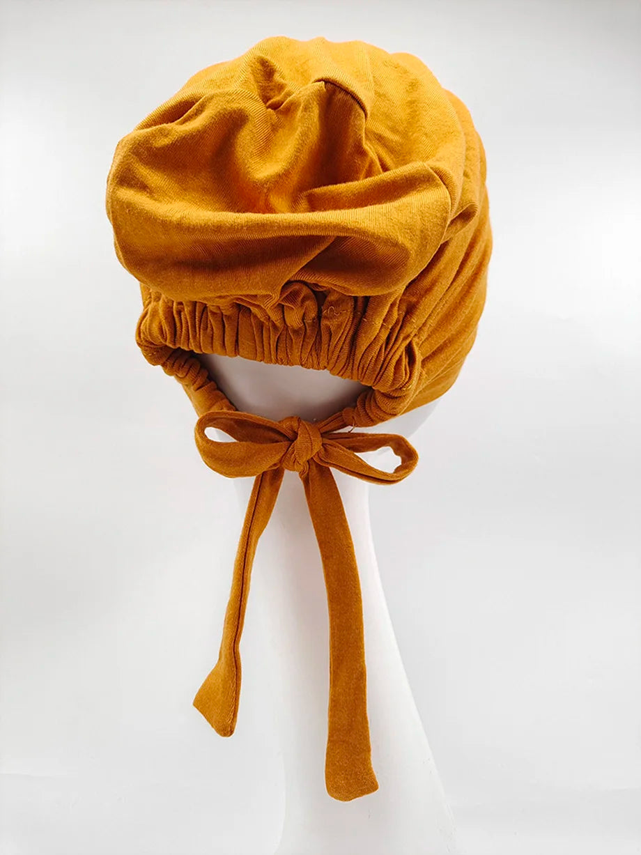 Pañuelo turbante de modal amarillo mostaza atado con cinta, exhibido en maniquí blanco.