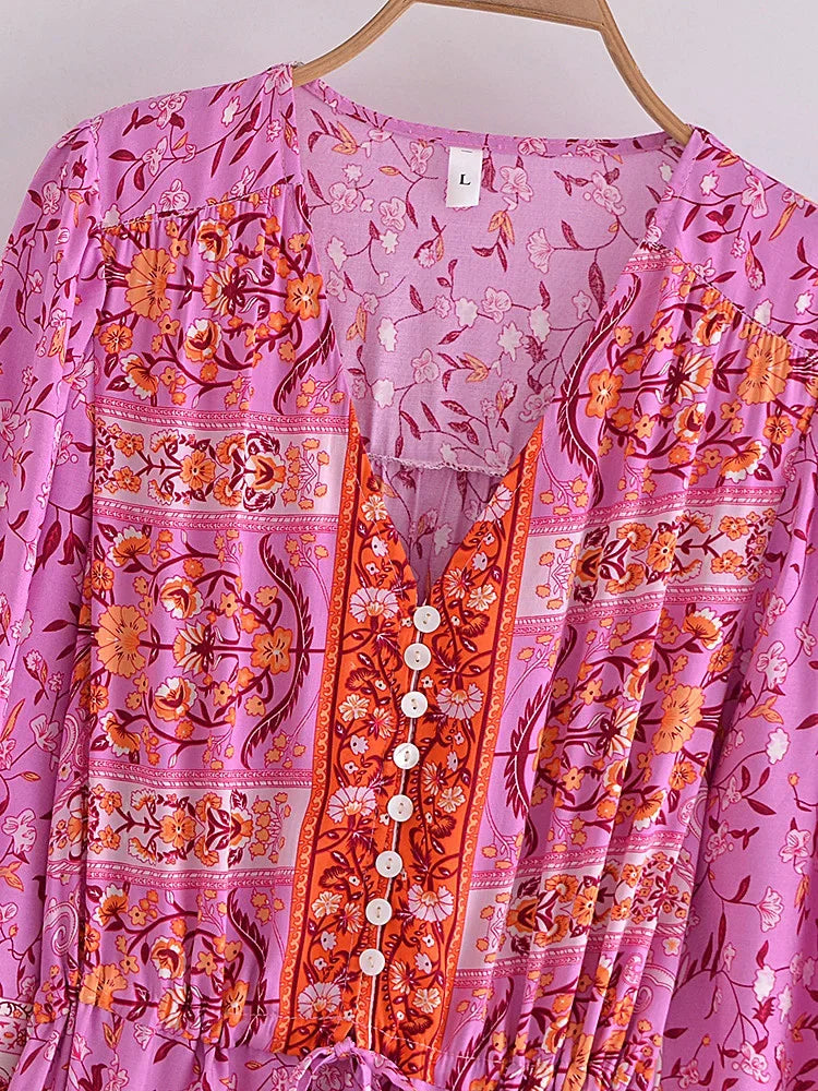 A pink floral maxi dress with orange embroidery and lantern sleeves displayed on a hanger.