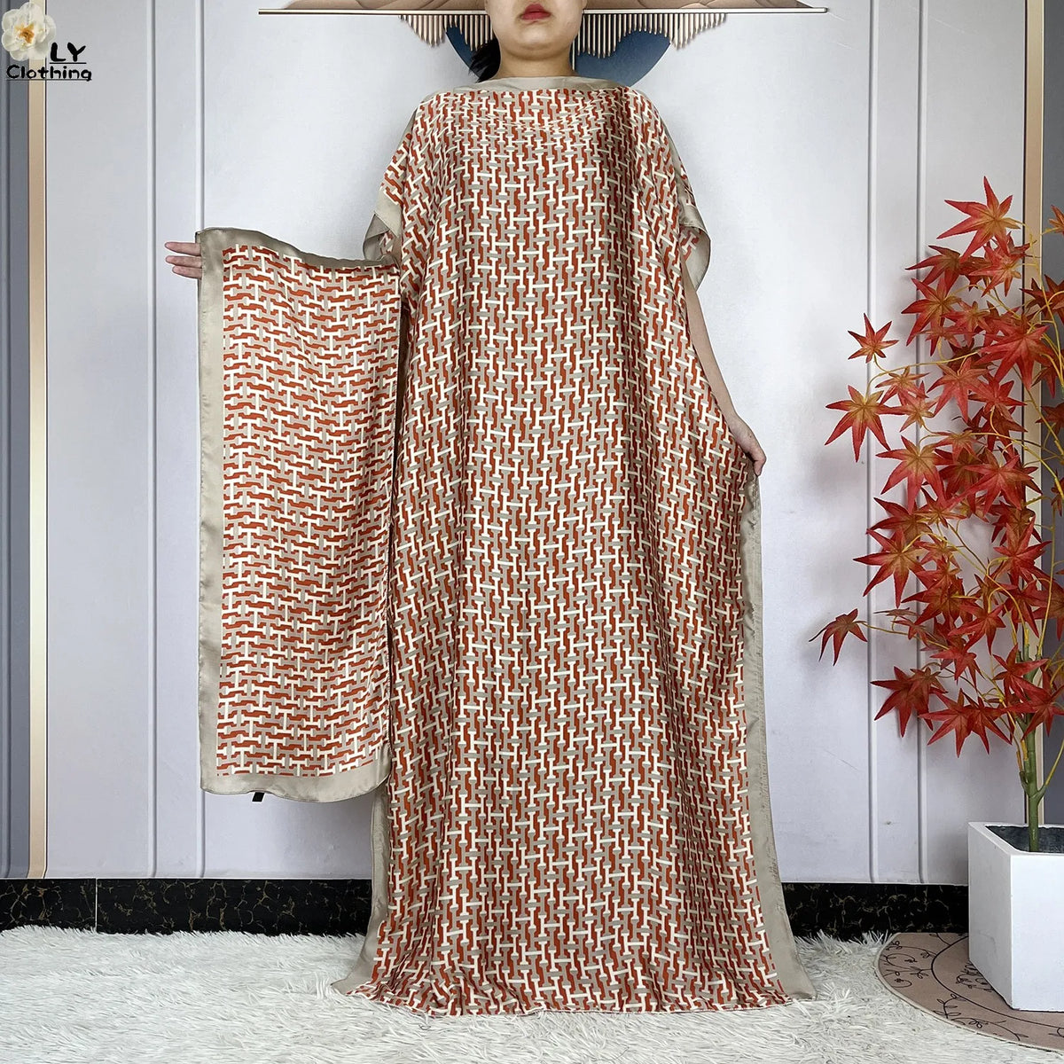 Model in a flowing, reddish-brown patterned kaftan dress with a sheer overlay and wide sleeve.