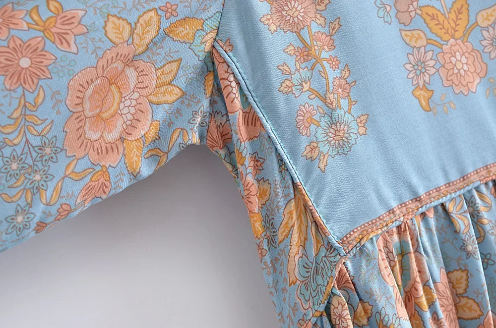 Close-up of a light blue bohemian floral maxi dress featuring detailed pink and yellow botanical print on the sleeve.