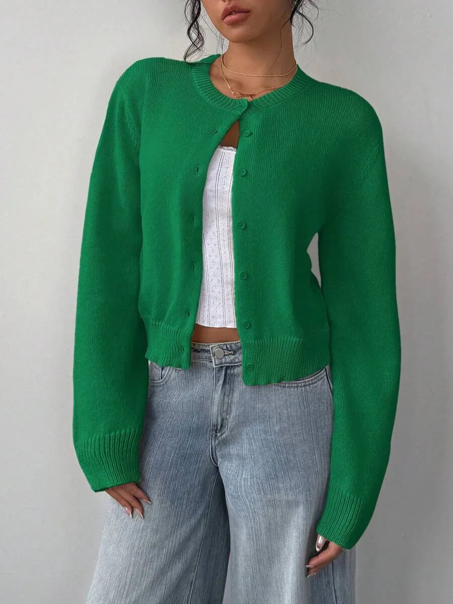 Une femme portant un pull-cardigan vert uni sur un haut blanc et un jean délavé clair.