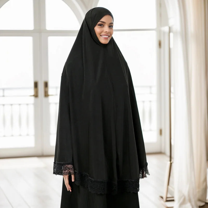 Eine Frau trägt einen schwarzen Instant-Hijab mit Spitzenrand, lächelt drinnen.