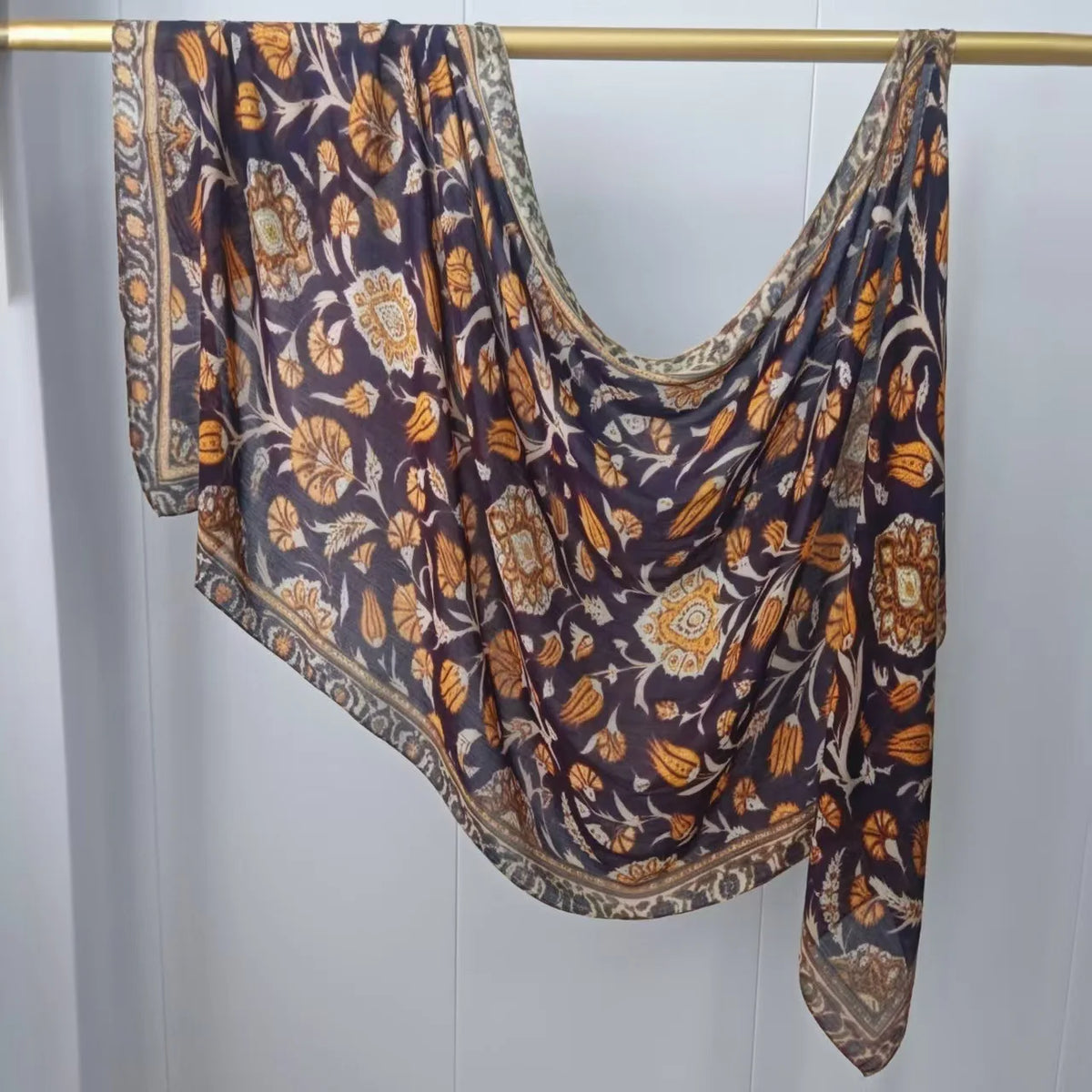 Dunkelviolettes und goldfarbenes gemustertes Hijab-Schal hängt an einem Holzbügel.