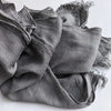Gros plan d'un foulard hijab en viscose coton gris avec pompons drapé sur une surface blanche.