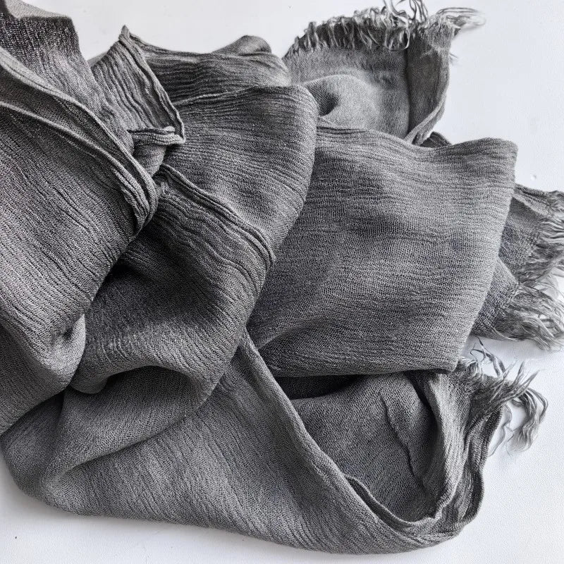 Gros plan d'un foulard hijab en viscose coton gris avec pompons drapé sur une surface blanche.