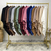A rack displaying numerous folded two-layer everyday hijab scarves in various shades of green, pink, brown, and blue.