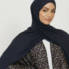 Eine Frau trägt einen dunkelblauen Jersey-Hijab und ein gemustertes Oberteil.